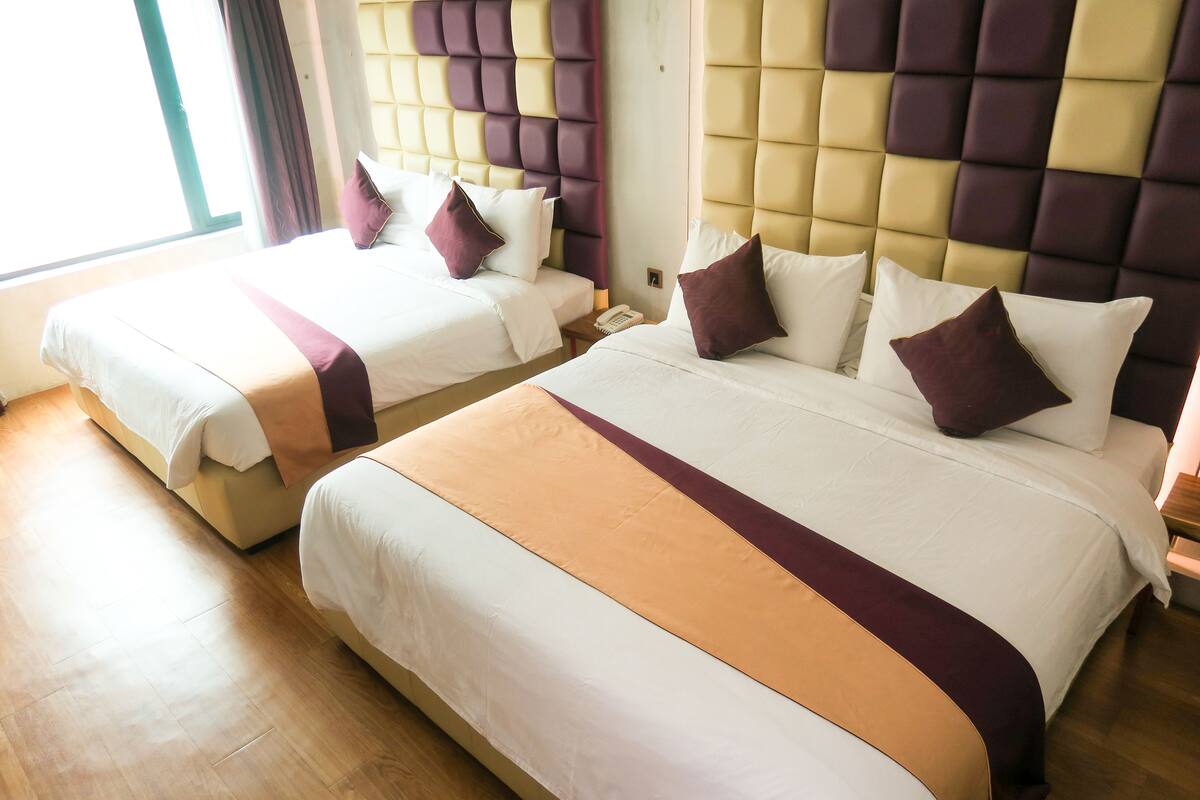 A hotel room with two beds, each with a headboard, a bedside table, and a telephone.