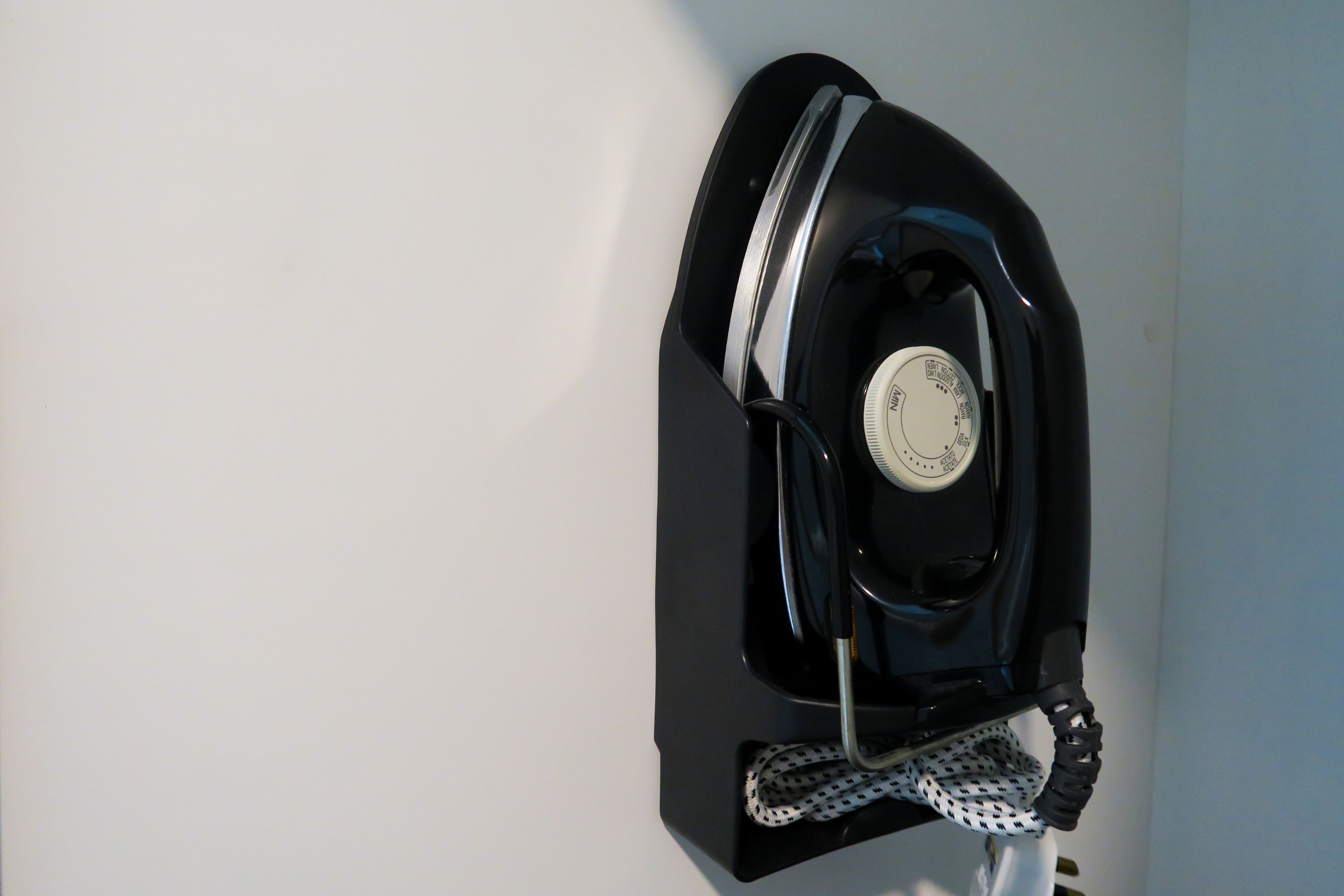 A wall-mounted iron with a control dial, a power cord, and a black and white patterned cloth.
