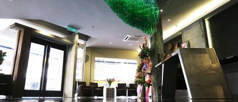 A lobby with a reflective floor, a green decorative ceiling feature, and a reception desk with chairs.