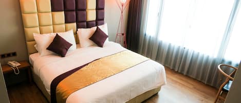 A hotel room with a large bed, a headboard with a geometric pattern, a bedside table with a phone, and a floor lamp.