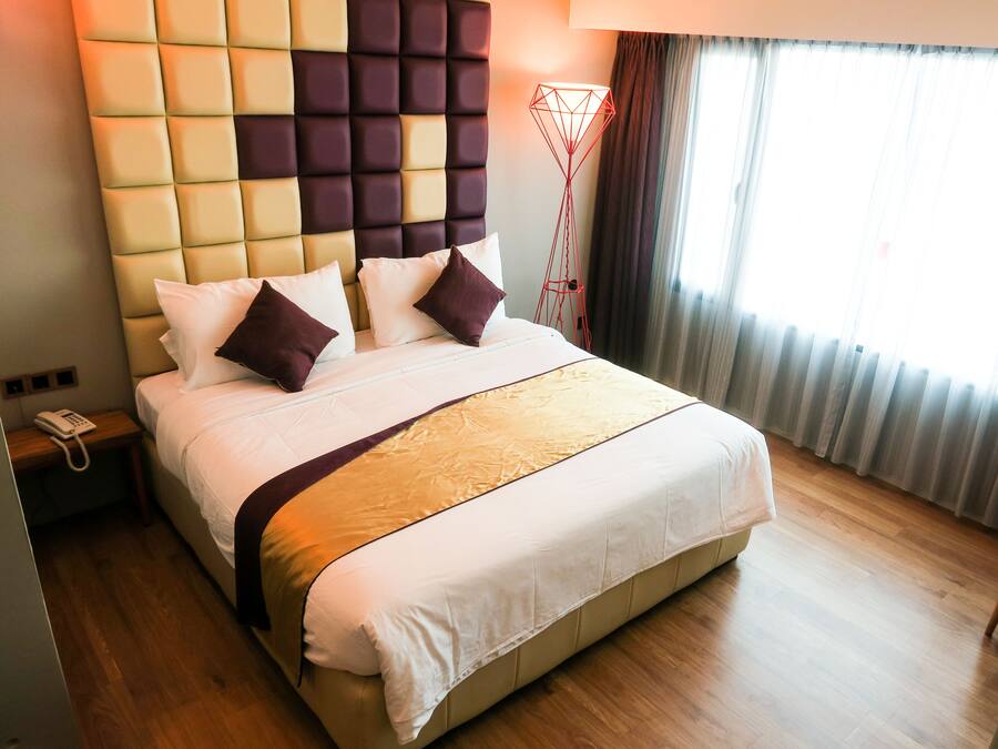 A hotel room with a large bed, a headboard with a geometric pattern, a bedside table with a phone, and a floor lamp.