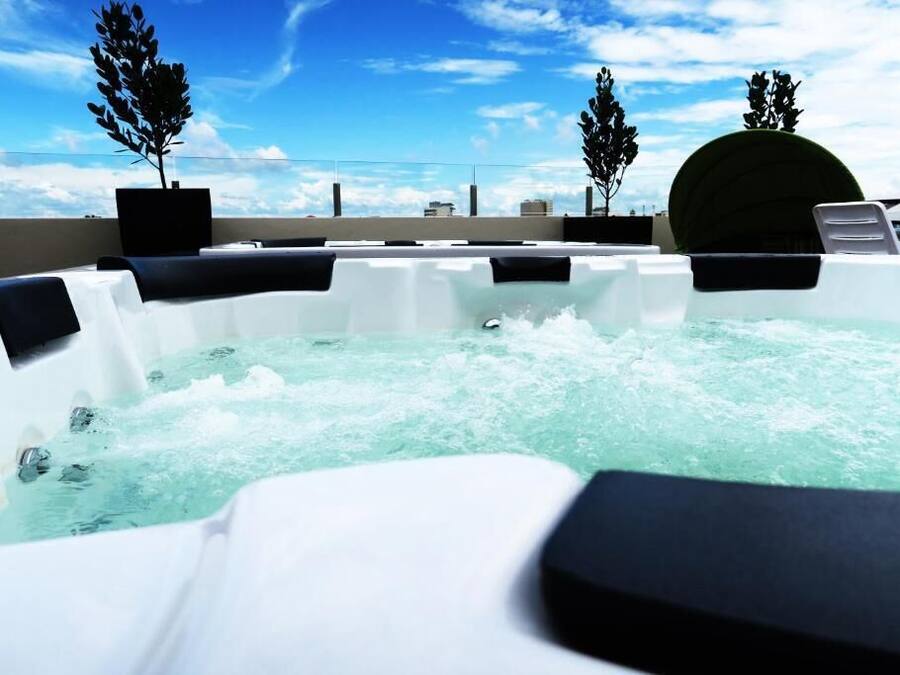 A hot tub with multiple seating areas, surrounded by potted plants and a clear sky.