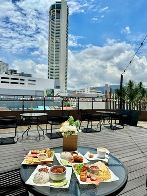A rooftop dining area with a variety of dishes, a table with chairs, and a view of a tall building in the background.