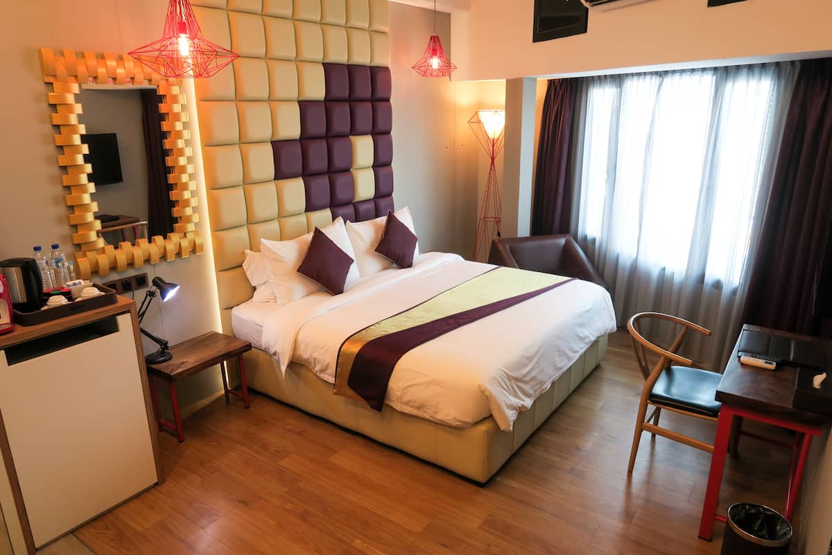 A hotel room with a bed, bedside table, desk, chair, and a TV.