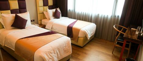 A hotel room with two beds, a wooden floor, a small table, and a trash bin.