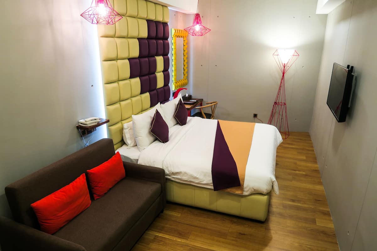 A modern hotel room with a bed, a sofa, a TV, and a unique wall design.