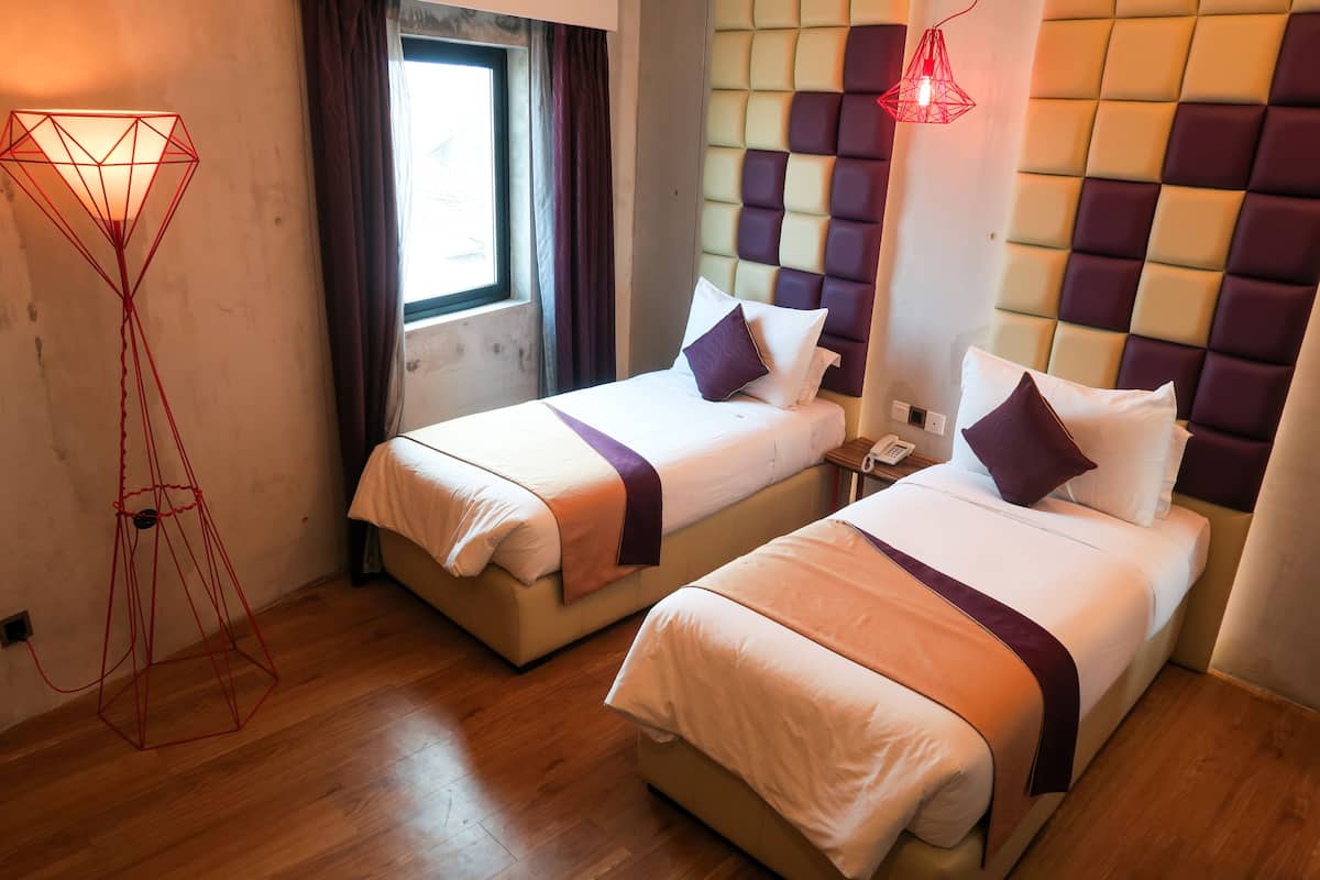 A hotel room with two beds, a window, a red floor lamp, and a modern headboard.
