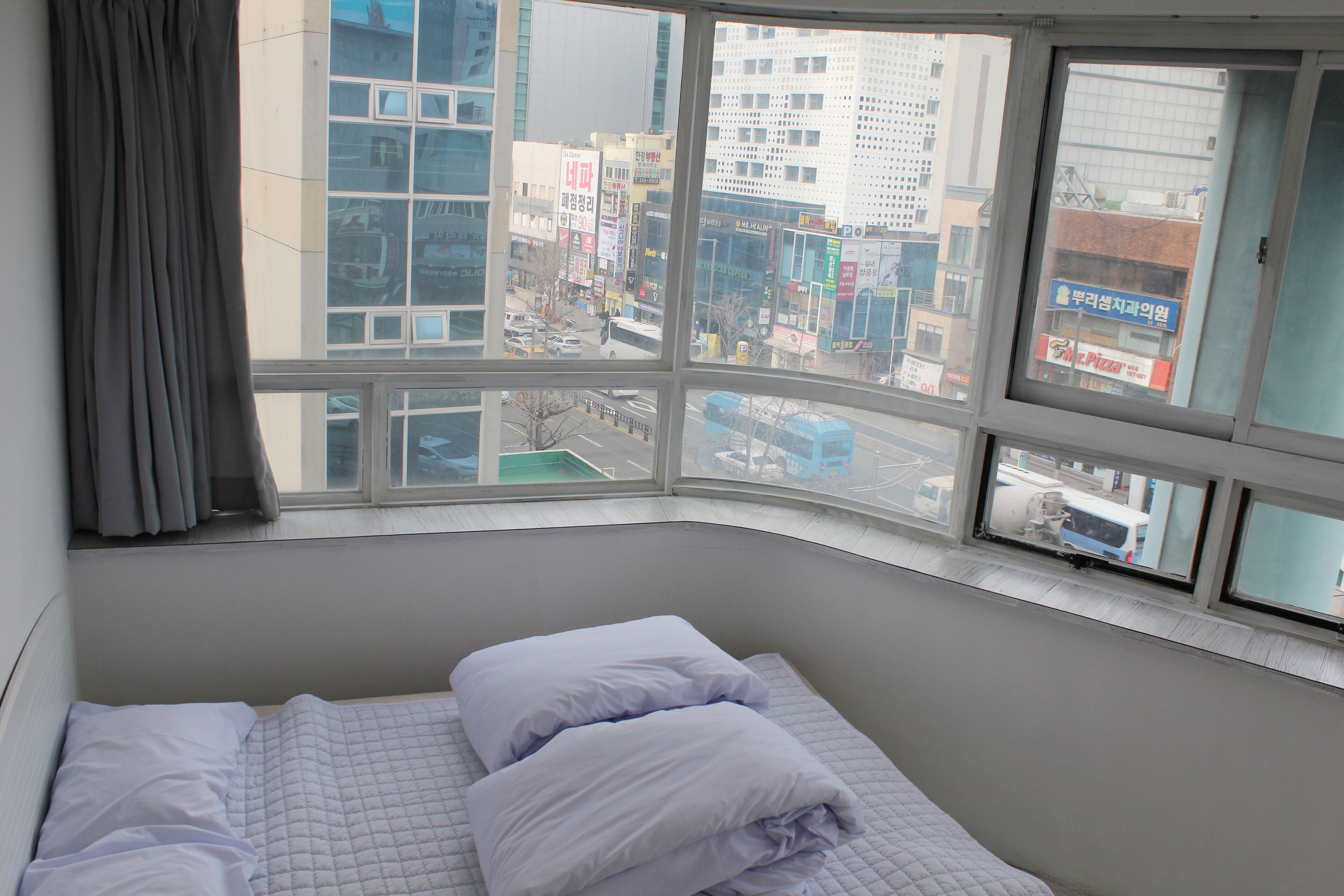 Ett hotellrum med en säng, ett fönster med utsikt över staden och en gardin.