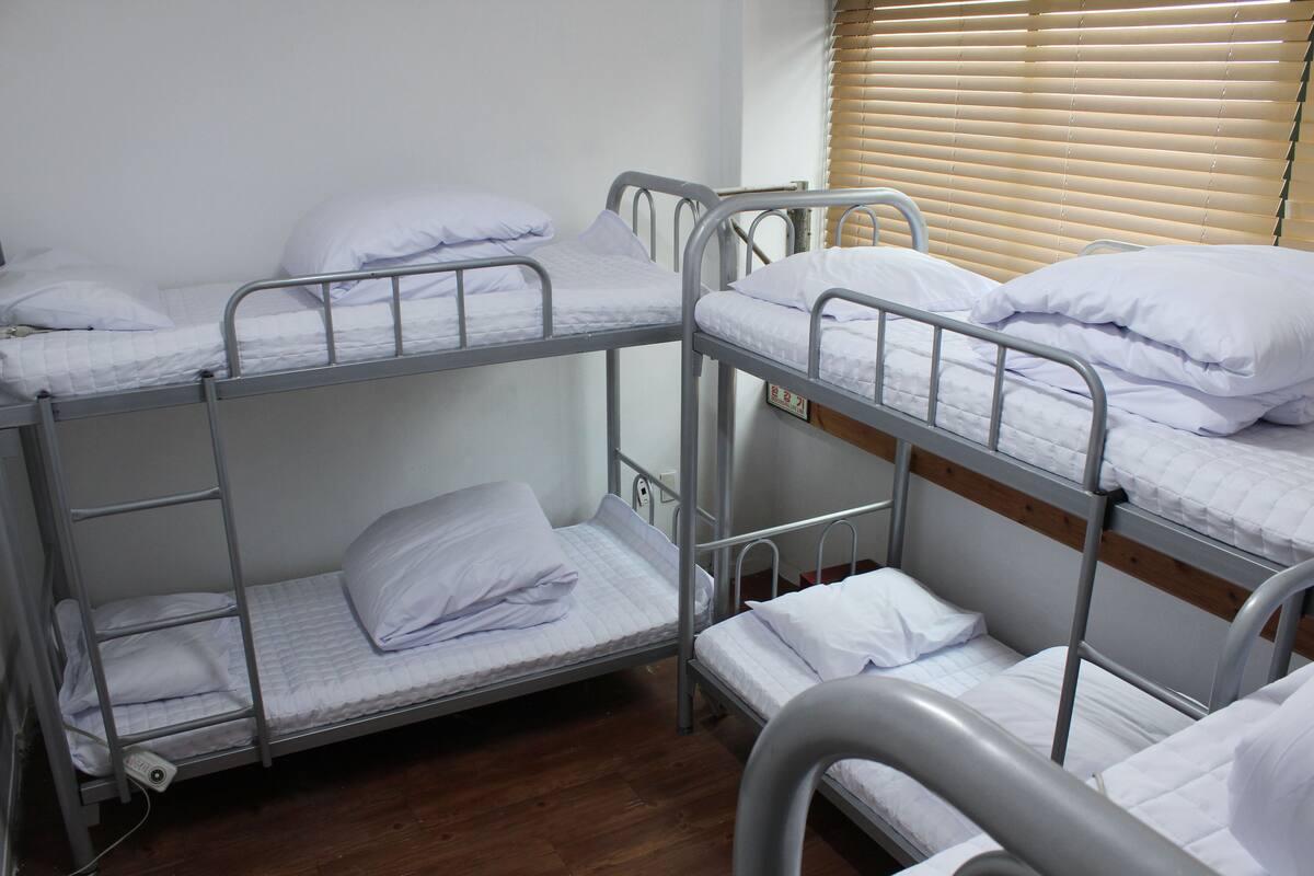 A bunk bed room with metal railings, white bedding, and a wooden floor.
