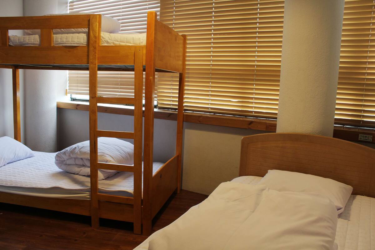 A bunk bed room with a wooden ladder, a window with blinds, and a wooden headboard.