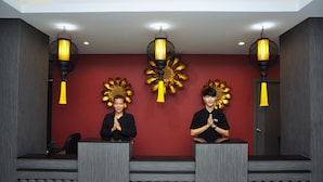 A reception area with two receptionists behind counters, red walls, and decorative golden sun-like wall art. - Chiangmai SP Hotel (Chiang Mai)