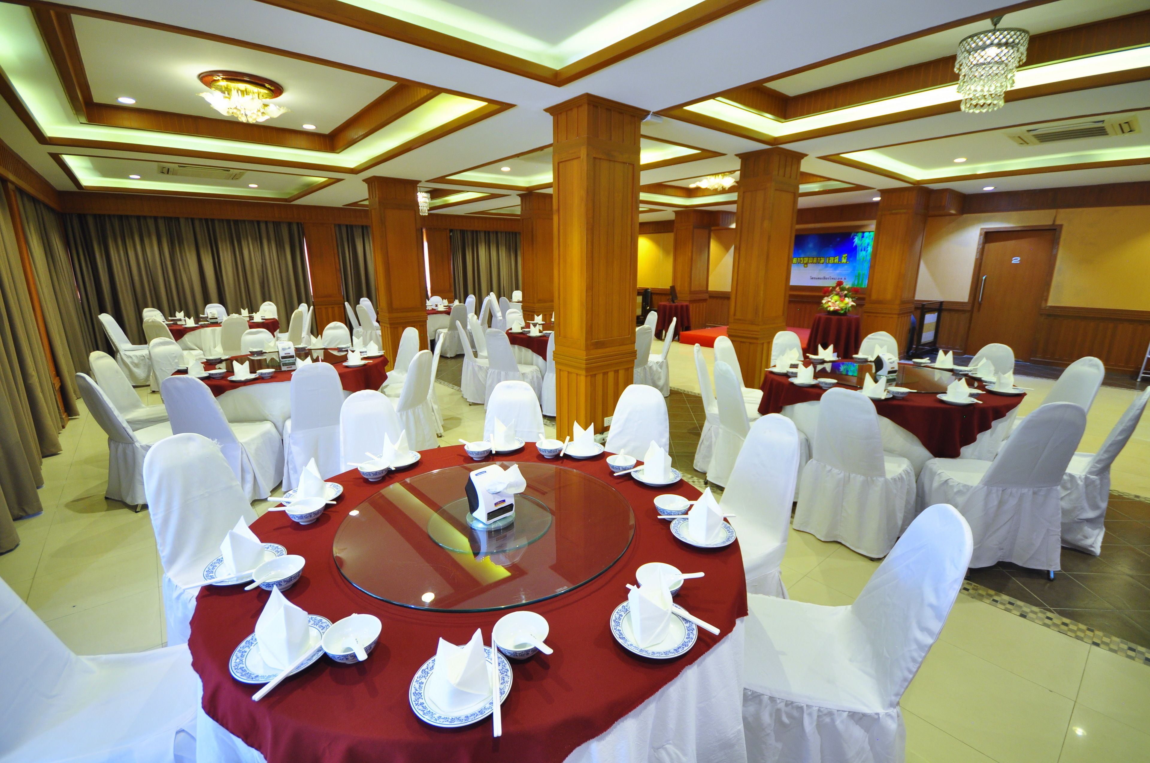 A banquet hall with round tables set for a formal event, featuring white chairs and red tablecloths.