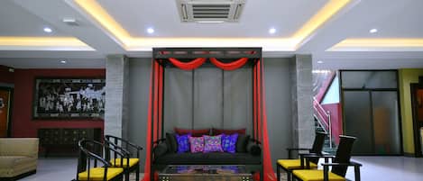 A modern lobby with a black sofa, yellow chairs, a patterned rug, and red curtains.