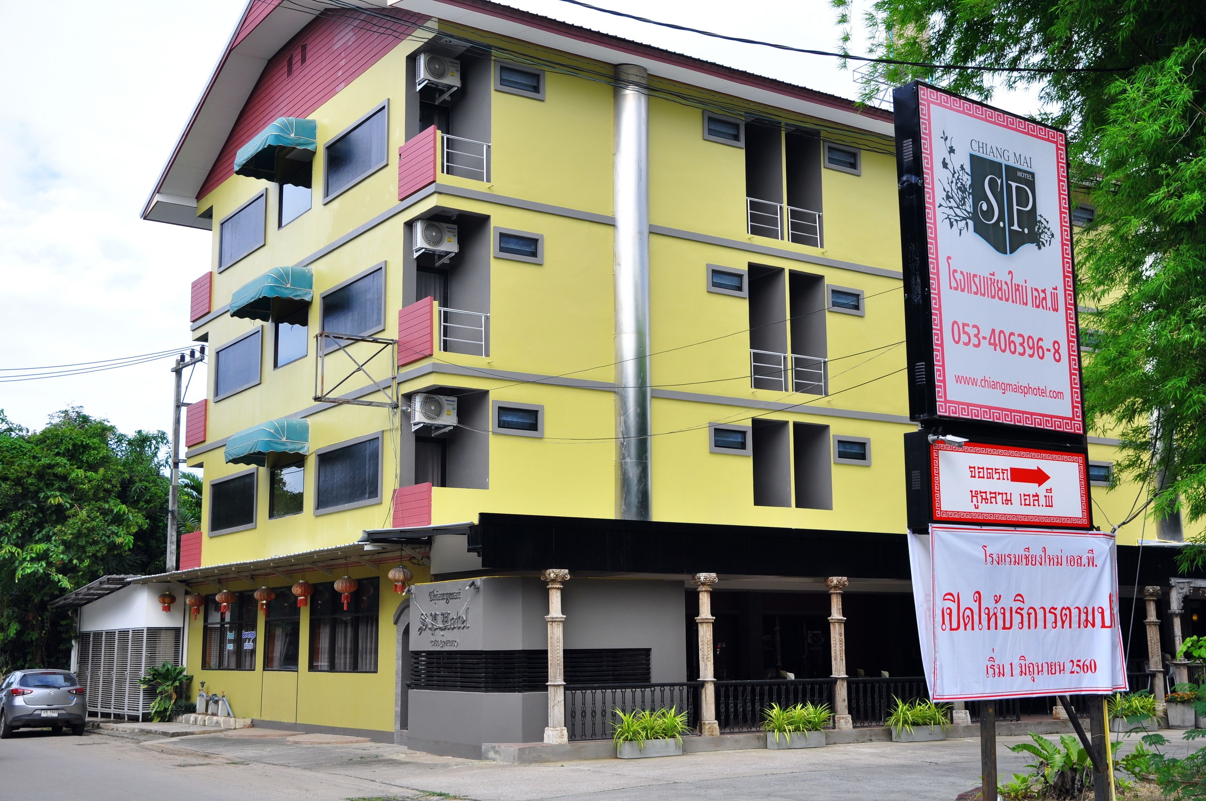 A multi-story hotel with balconies, air conditioning units, and a prominent signage for 'Chong Mai S.P.' with contact information and a website URL.