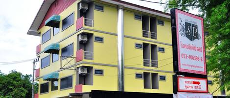 Un hotel de varios pisos con balcones, unidades de aire acondicionado y una señalización destacada que dice 'Chong Mai S.P.', con información de contacto y una URL de sitio web.