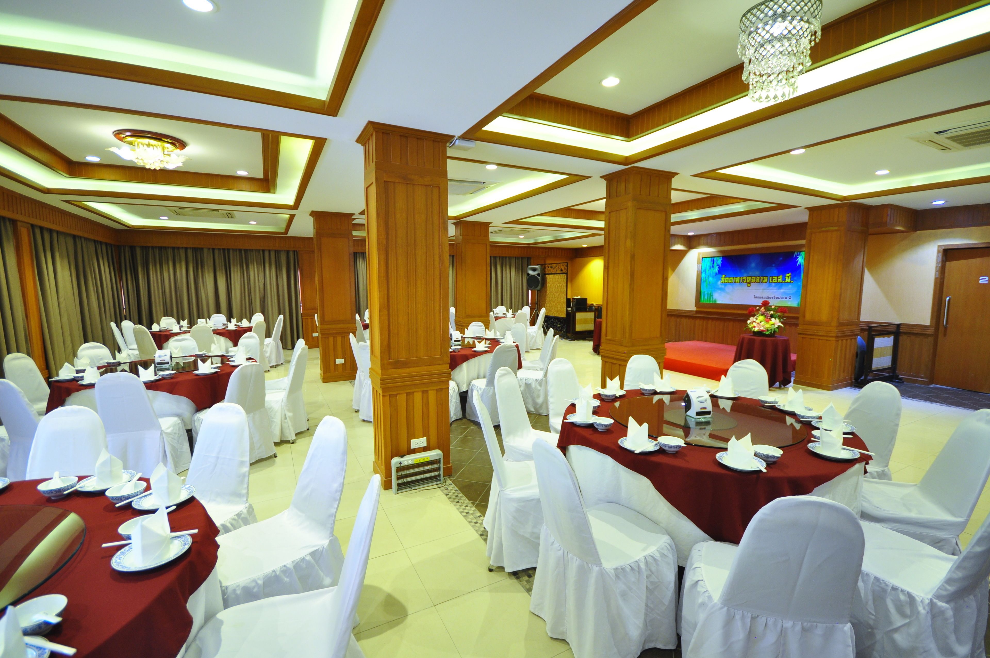 A banquet hall with round tables set for dining, white chairs, and a large screen in the background.