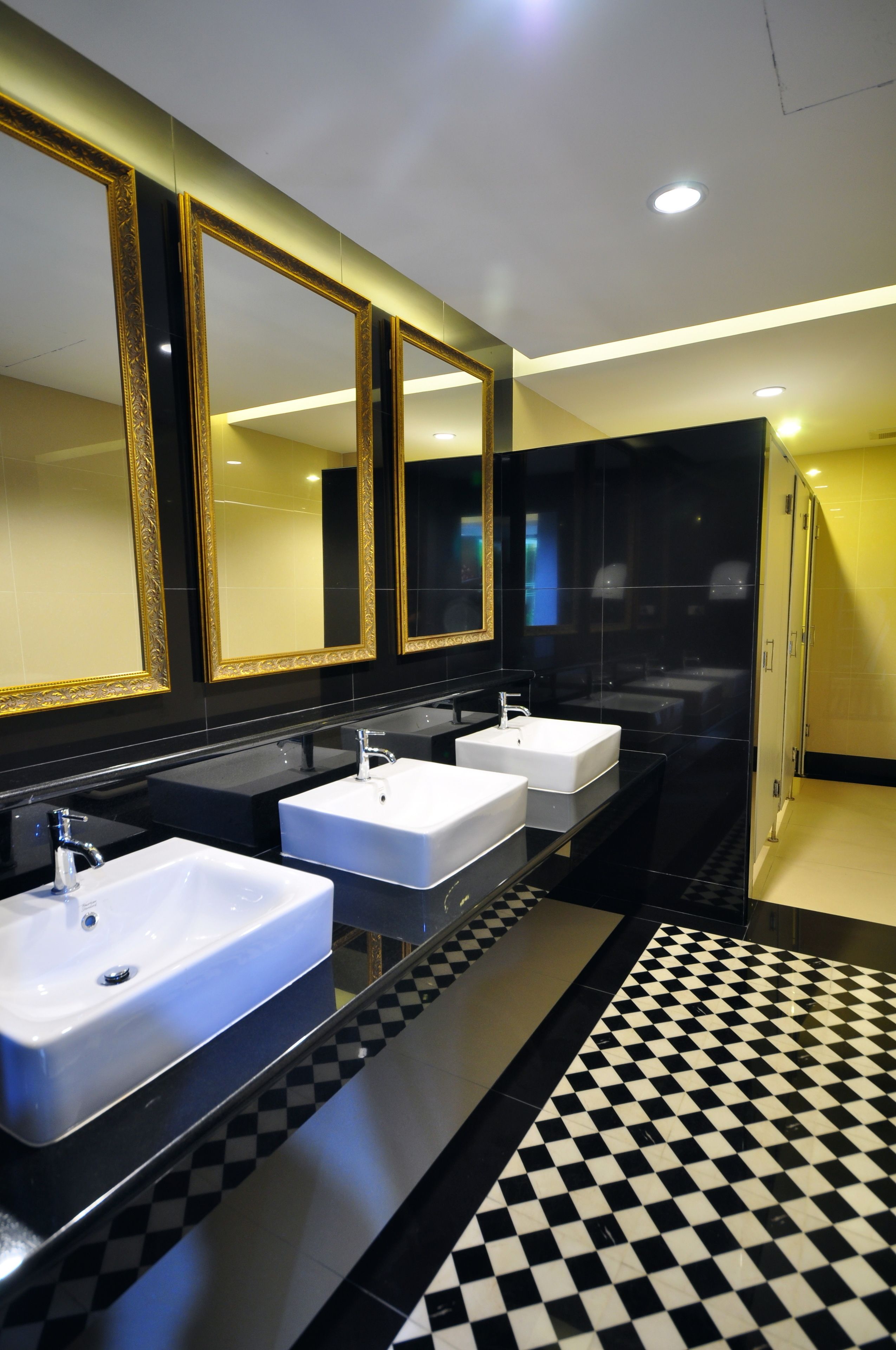 A modern bathroom with three white sinks, black countertops, and gold-framed mirrors.