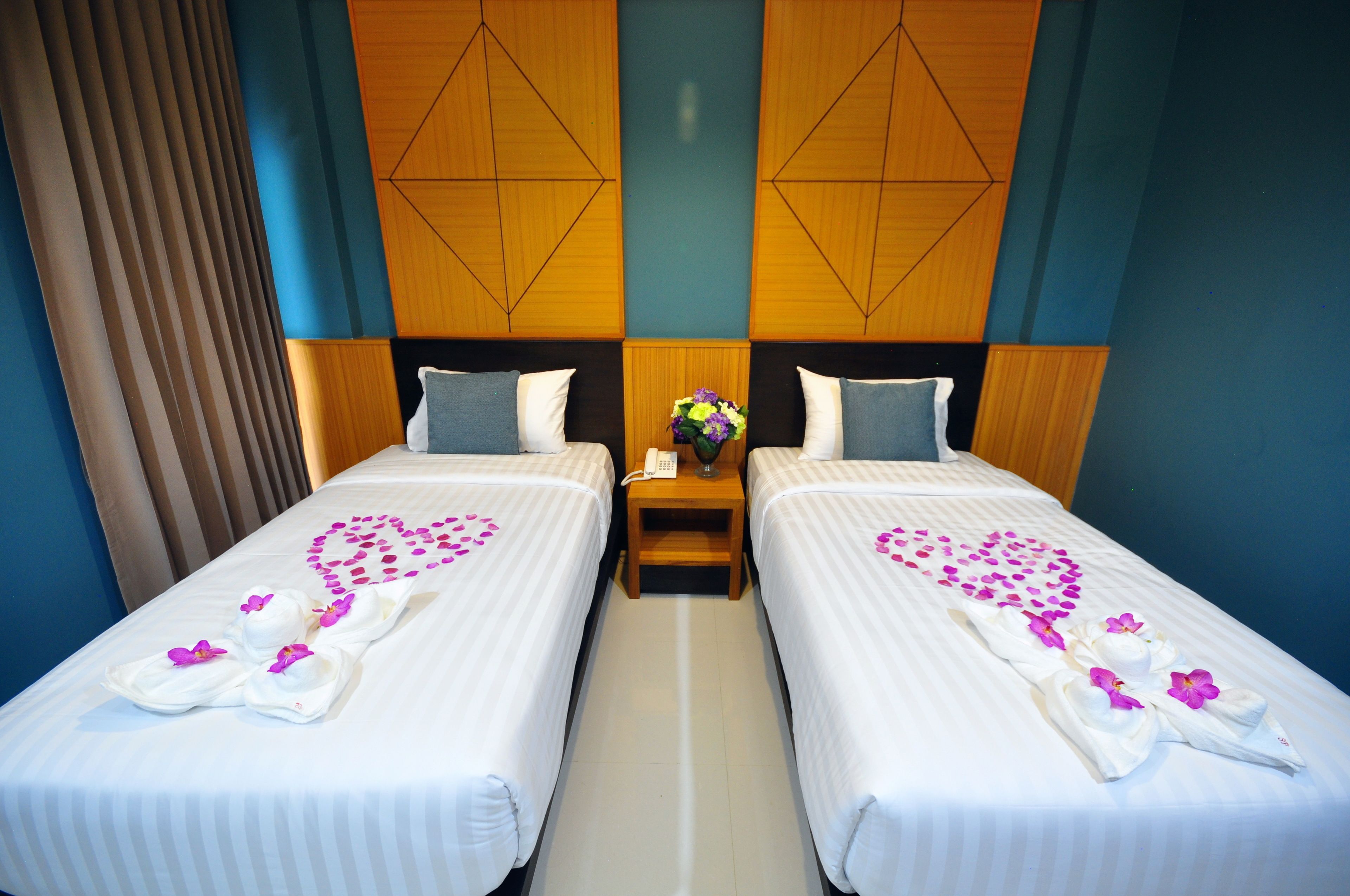 Ein Hotelzimmer mit zwei Betten, jedes mit einer herzförmigen Blumenkomposition und Handtüchern.