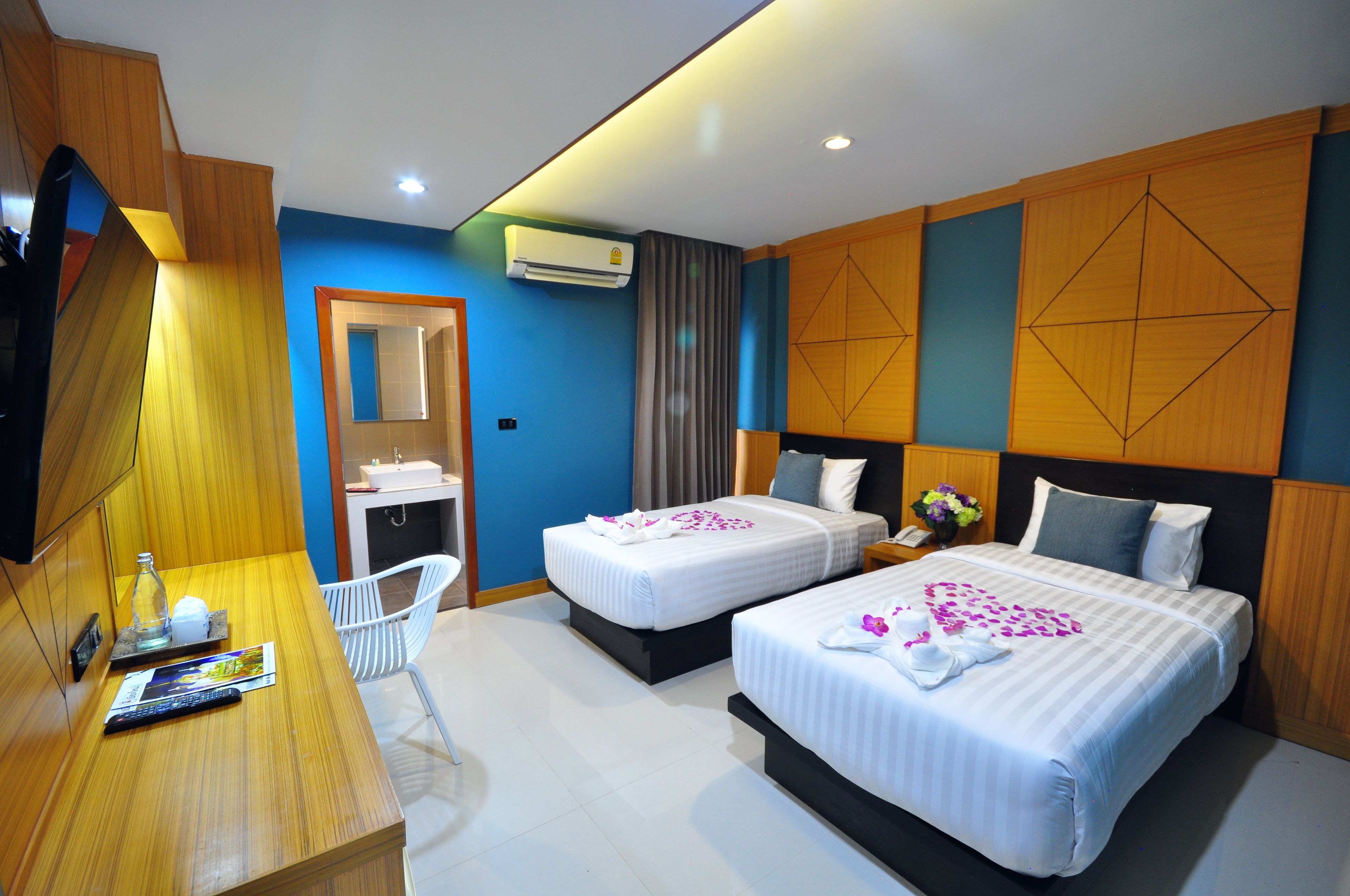 A hotel room with two beds, a desk with a chair, a mirror, and an air conditioning unit.