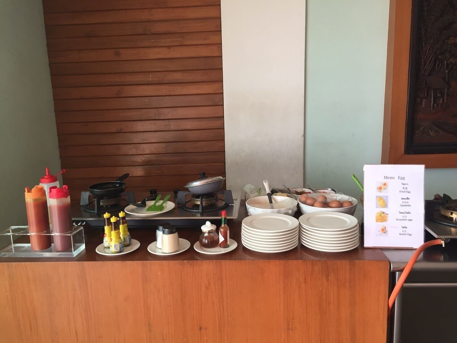 A buffet setup with condiments, plates, and a menu board.