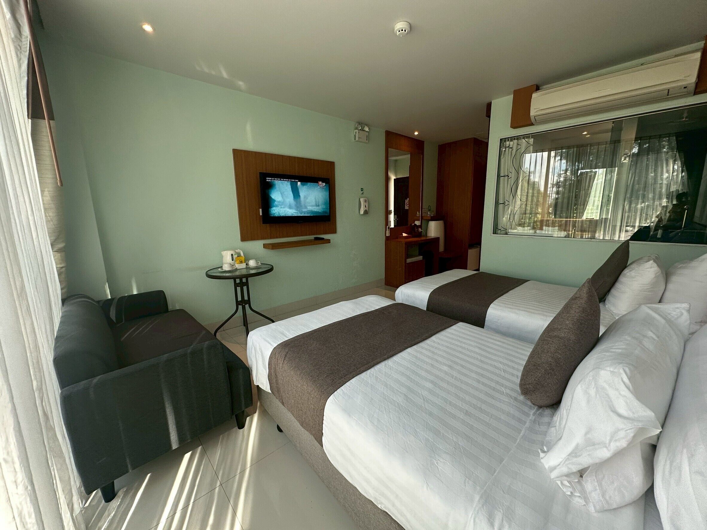 Habitación de hotel con dos camas, un televisor, una mesita con cafetera y una ventana con cortinas.