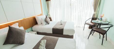 A hotel room with two beds, a small table with a chair, and a window with curtains.