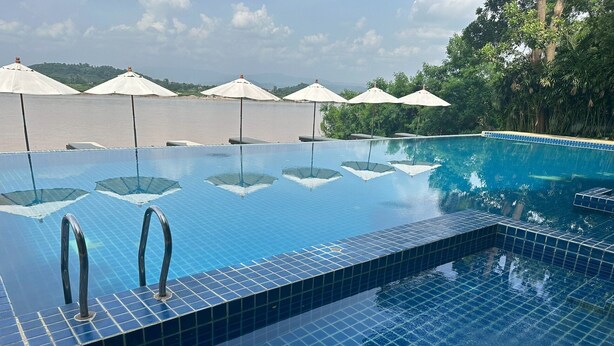 Una piscina infinita azul cristalina con borde de azulejos, rodeada de sombrillas blancas y árboles.