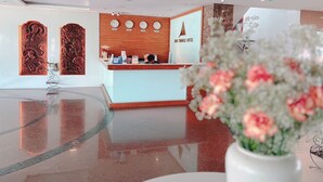 Zona de recepción de hotel con piso de mármol pulido, mostrador de recepción y paneles decorativos tradicionales.