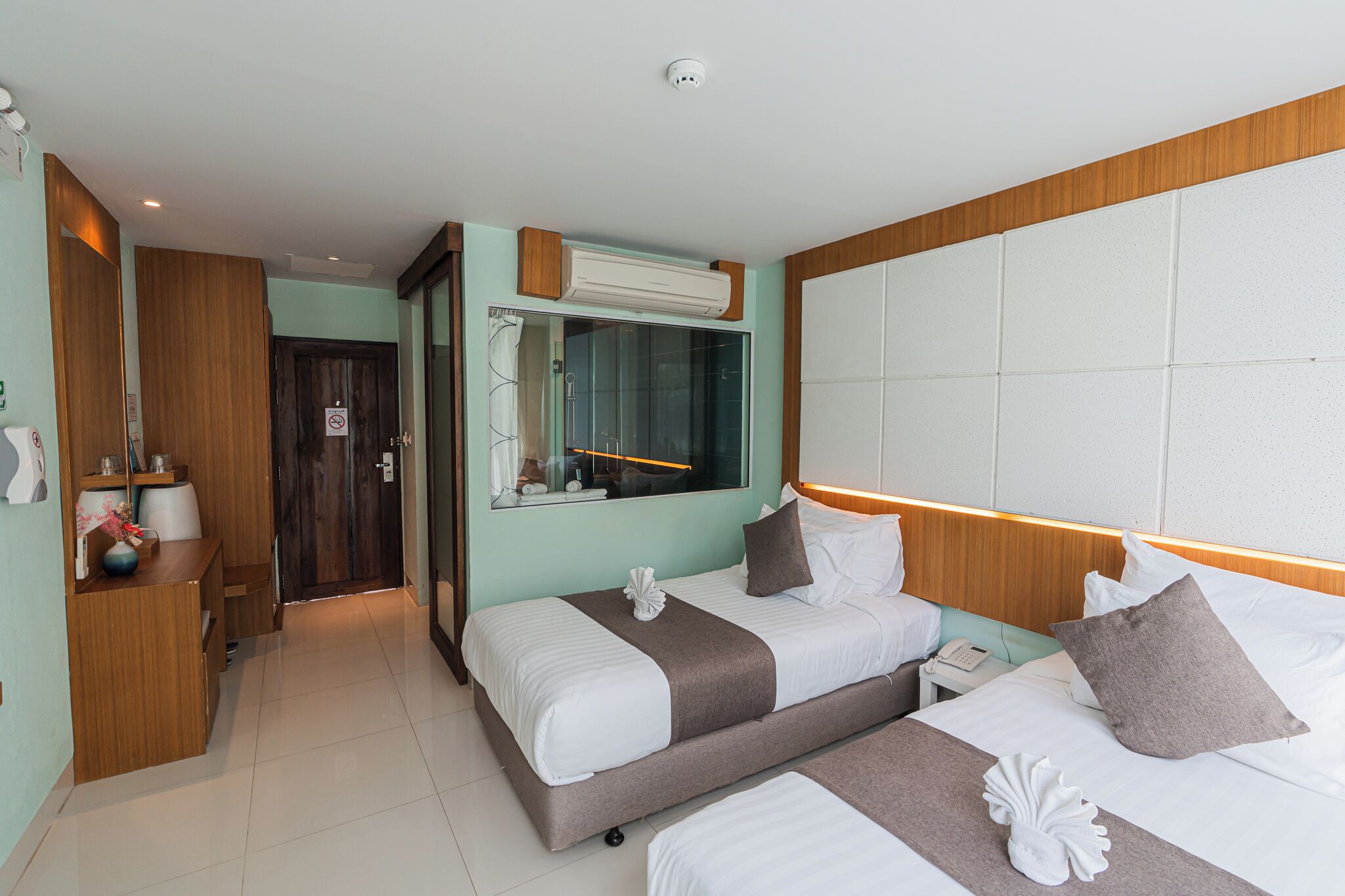 Habitación de hotel con dos camas, cabecero de madera, un espejo grande y aire acondicionado instalado.