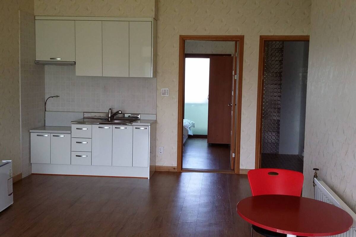 Eine kleine Küche mit weißen Schränken, einer Edelstahl-Spüle und einem roten Tisch.