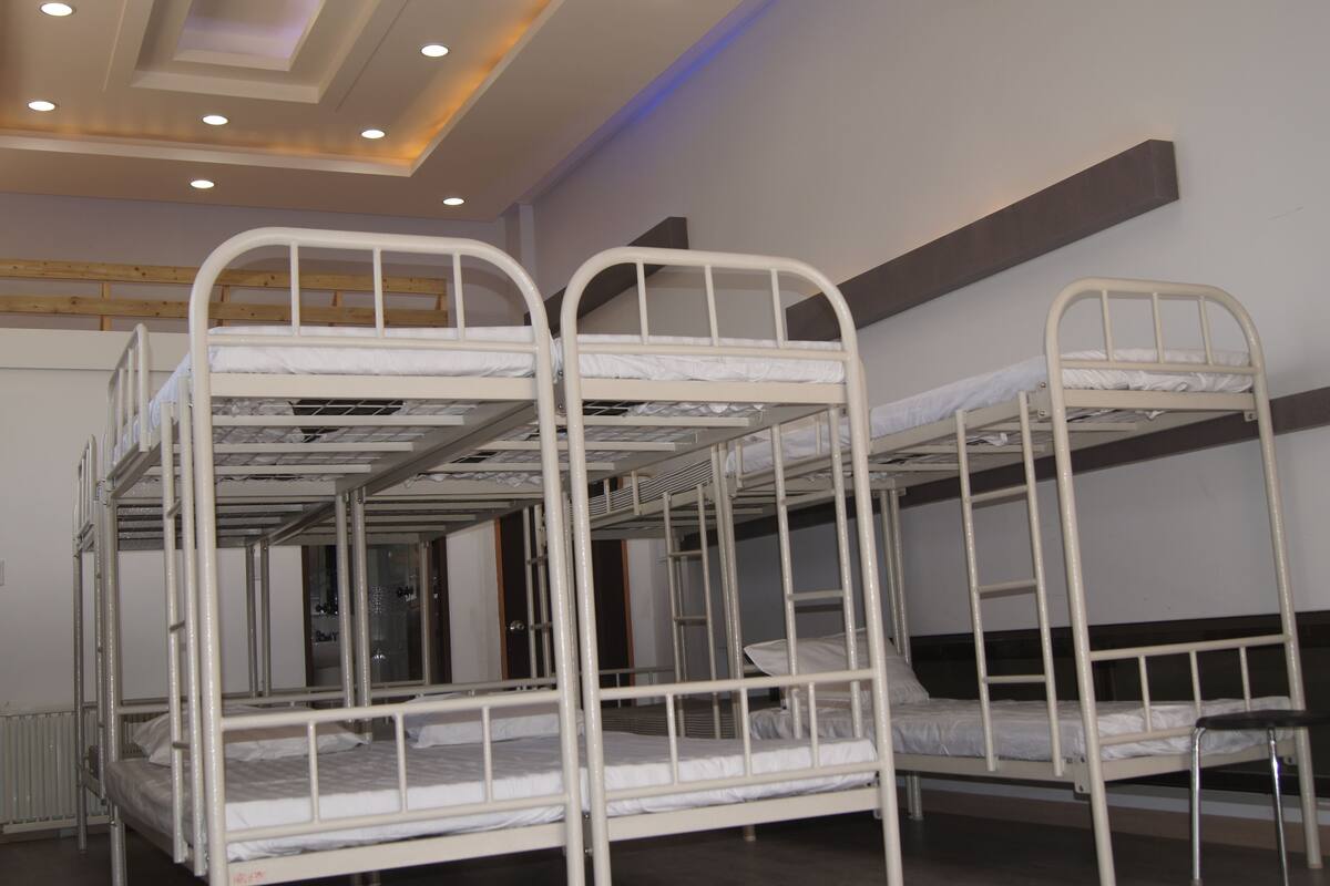 Ein Schlafsaalzimmer mit Etagenbetten, Holzvertäfelung an den Wänden und einer Decke mit eingelassenen Leuchten.