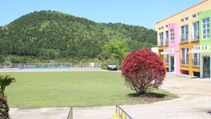 A building with a flat roof and a large open grassy area in front. - Geomunoreum Hostel (Jeju City)