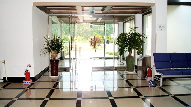A modern lobby with a checkered floor, potted plants, a blue seating area, and a glass door leading outside. - Geomunoreum Hostel (Jeju City)