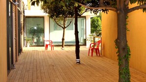 A wooden deck with two red chairs and a tree in a courtyard. - Geomunoreum Hostel (Jeju City)