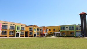 A row of colorful buildings with a central tower, a grassy courtyard, and a clear blue sky. - Geomunoreum Hostel (Jeju City)