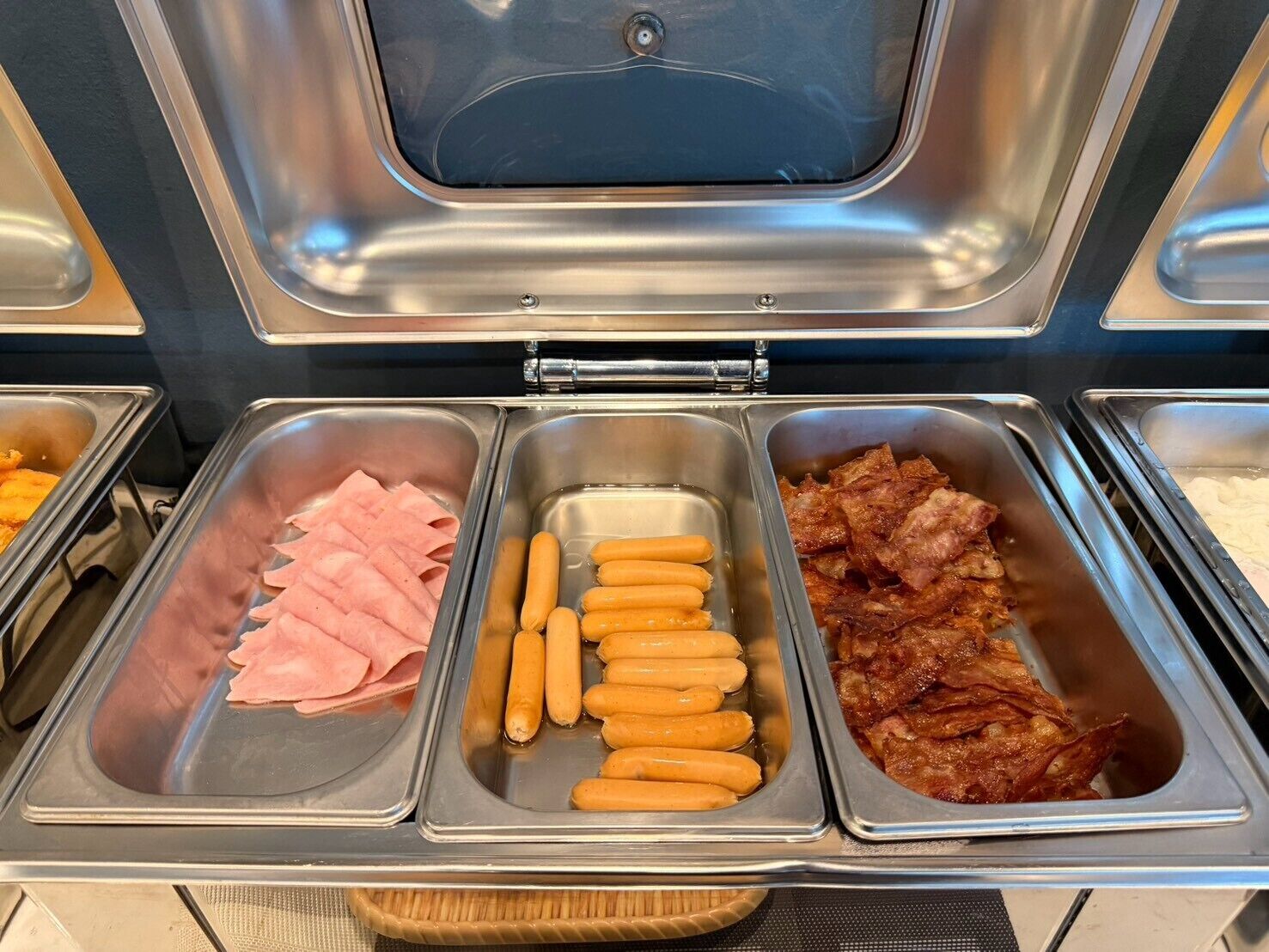 A buffet with various food options including sliced ham, sausages, and bacon.