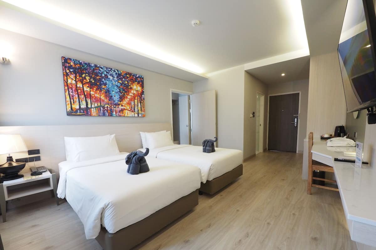 Habitación de hotel con dos camas, un escritorio, un televisor y un cuadro en la pared.