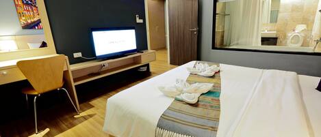 Habitación de hotel con una cama, un escritorio, una silla, un televisor y un espejo grande.