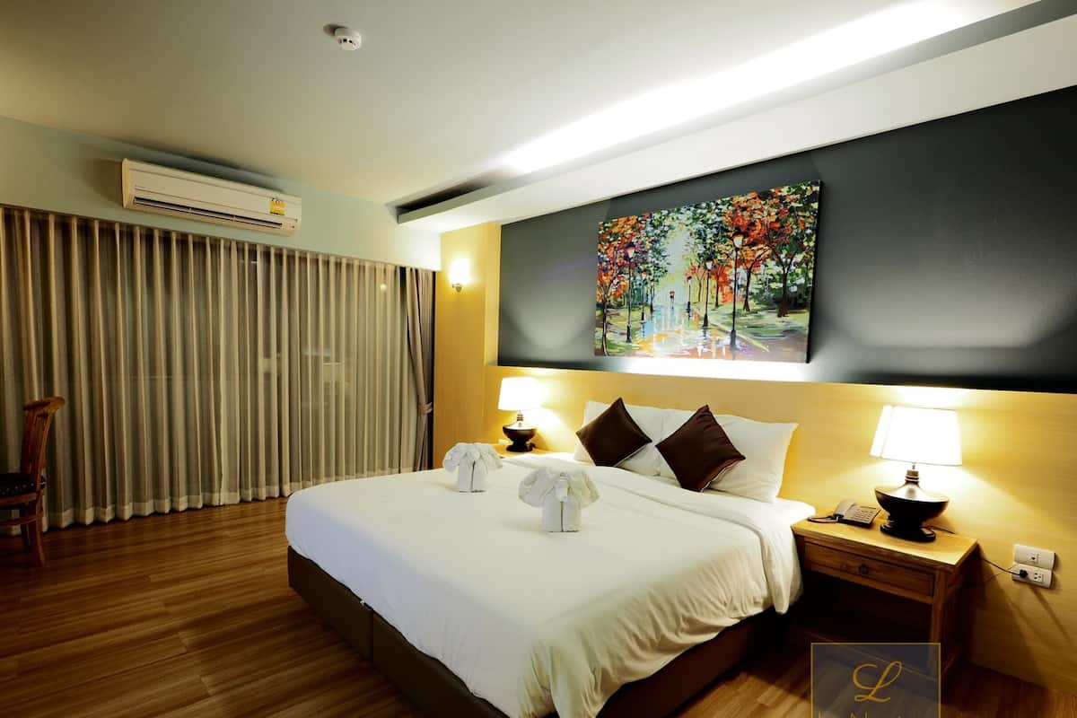 Habitación de hotel con una cama grande, un cuadro en la pared, una mesita de noche con lámpara y un equipo de aire acondicionado.