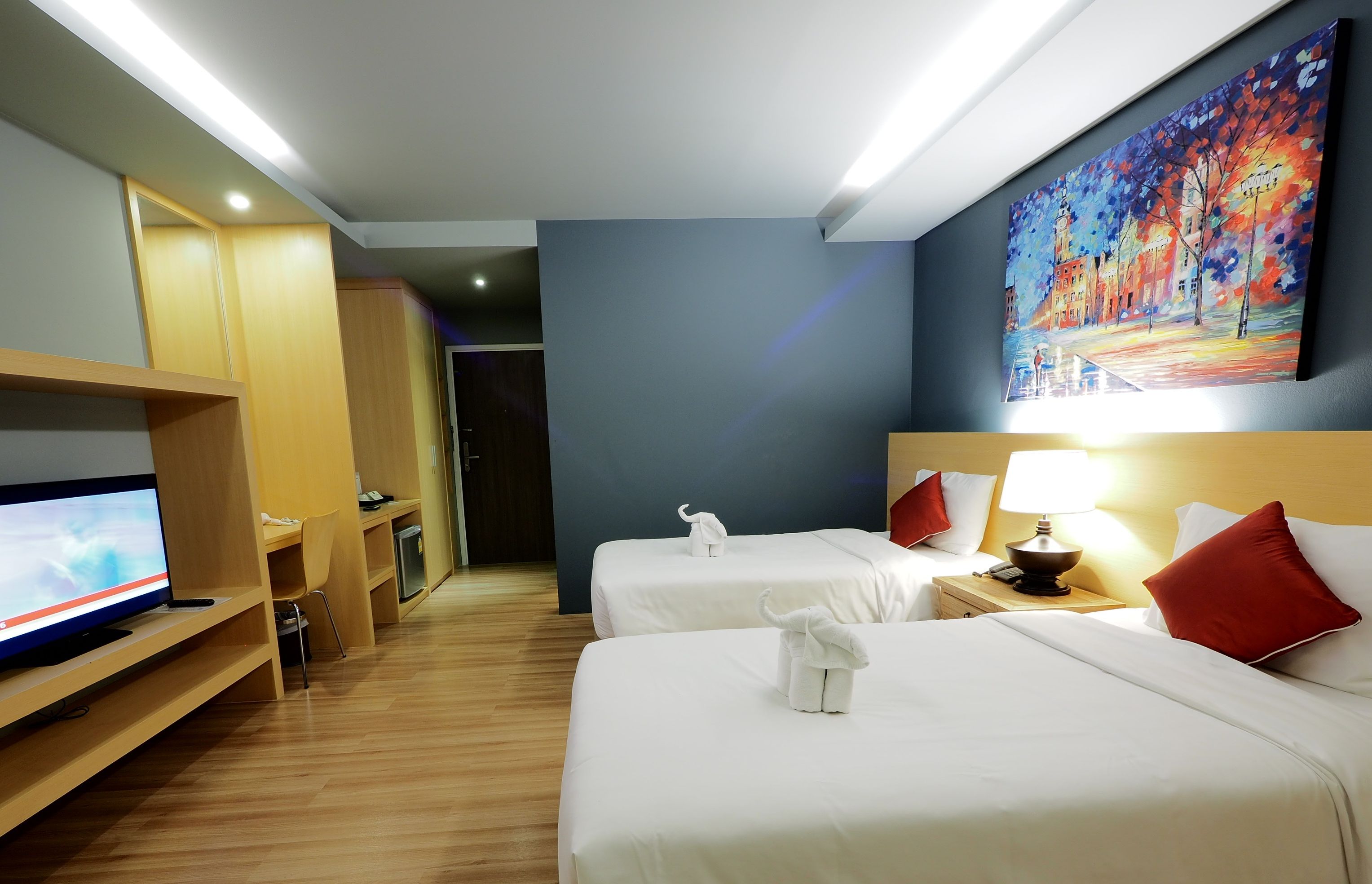 Habitación de hotel con dos camas, un televisor en un estante, un cuadro en la pared y un escritorio con una silla.