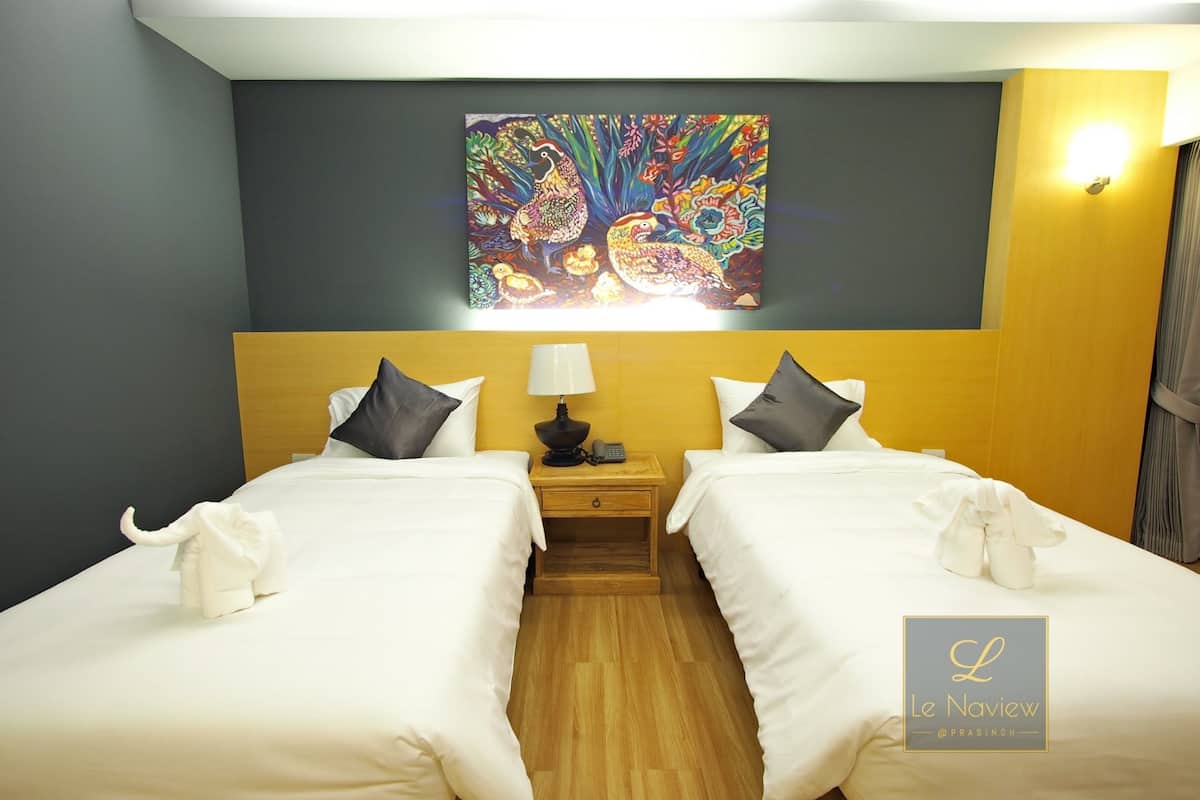 Habitación de hotel con dos camas, una mesita de noche con lámpara, un cuadro sobre las camas y un logotipo en la pared.