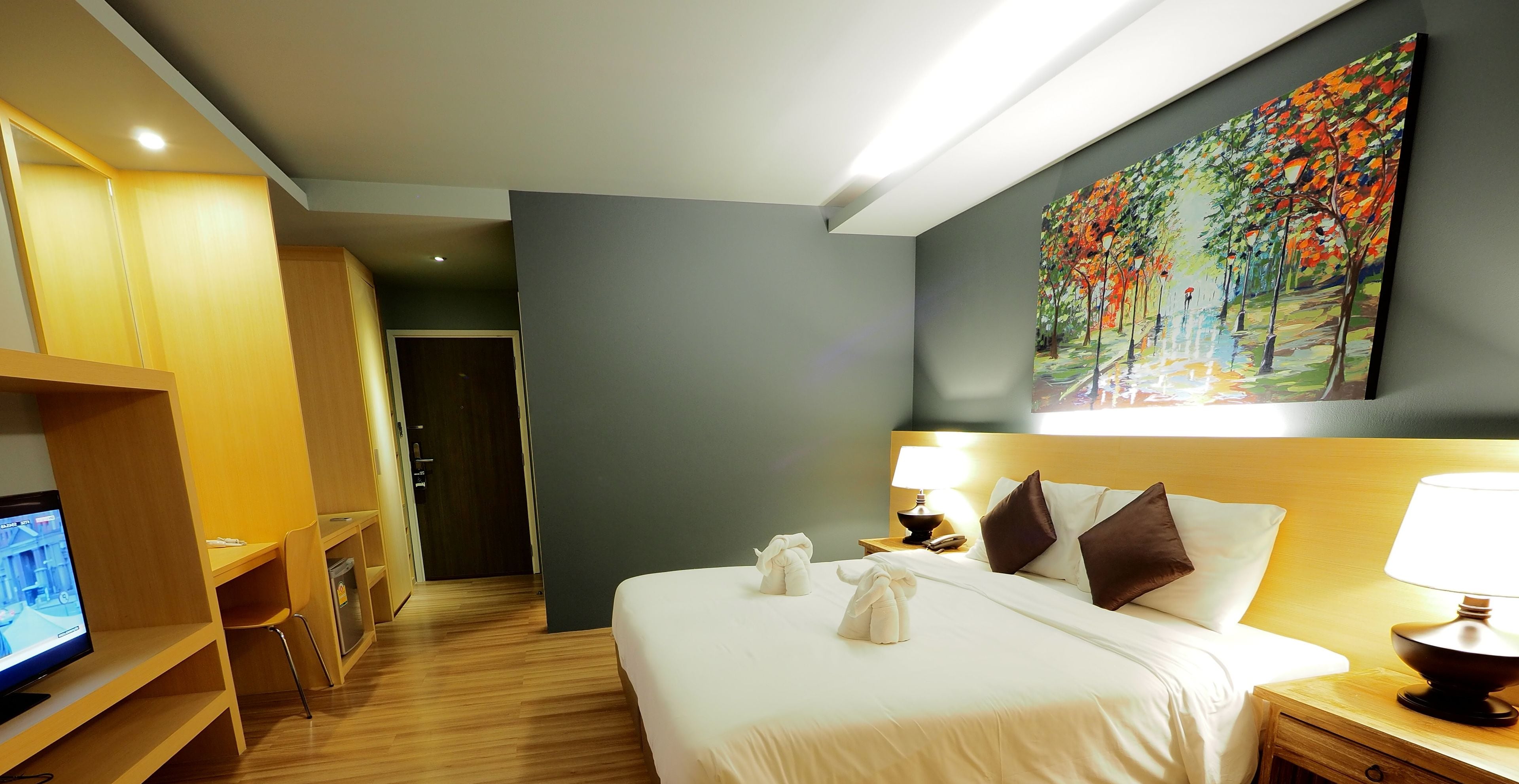 A hotel room with a bed, bedside table, lamp, and a painting on the wall.