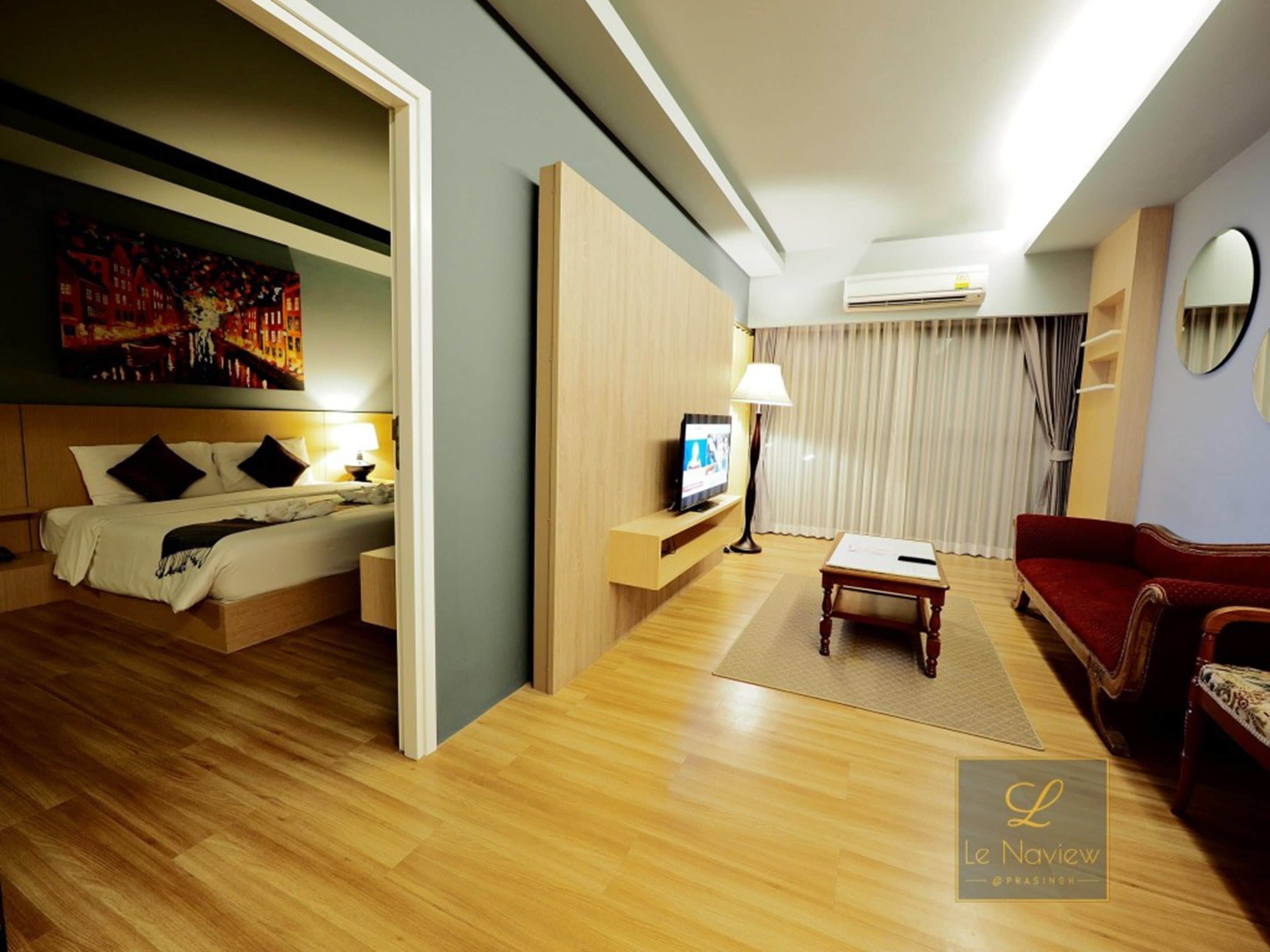 A hotel room with a bed, a TV, a sofa, and a painting on the wall.