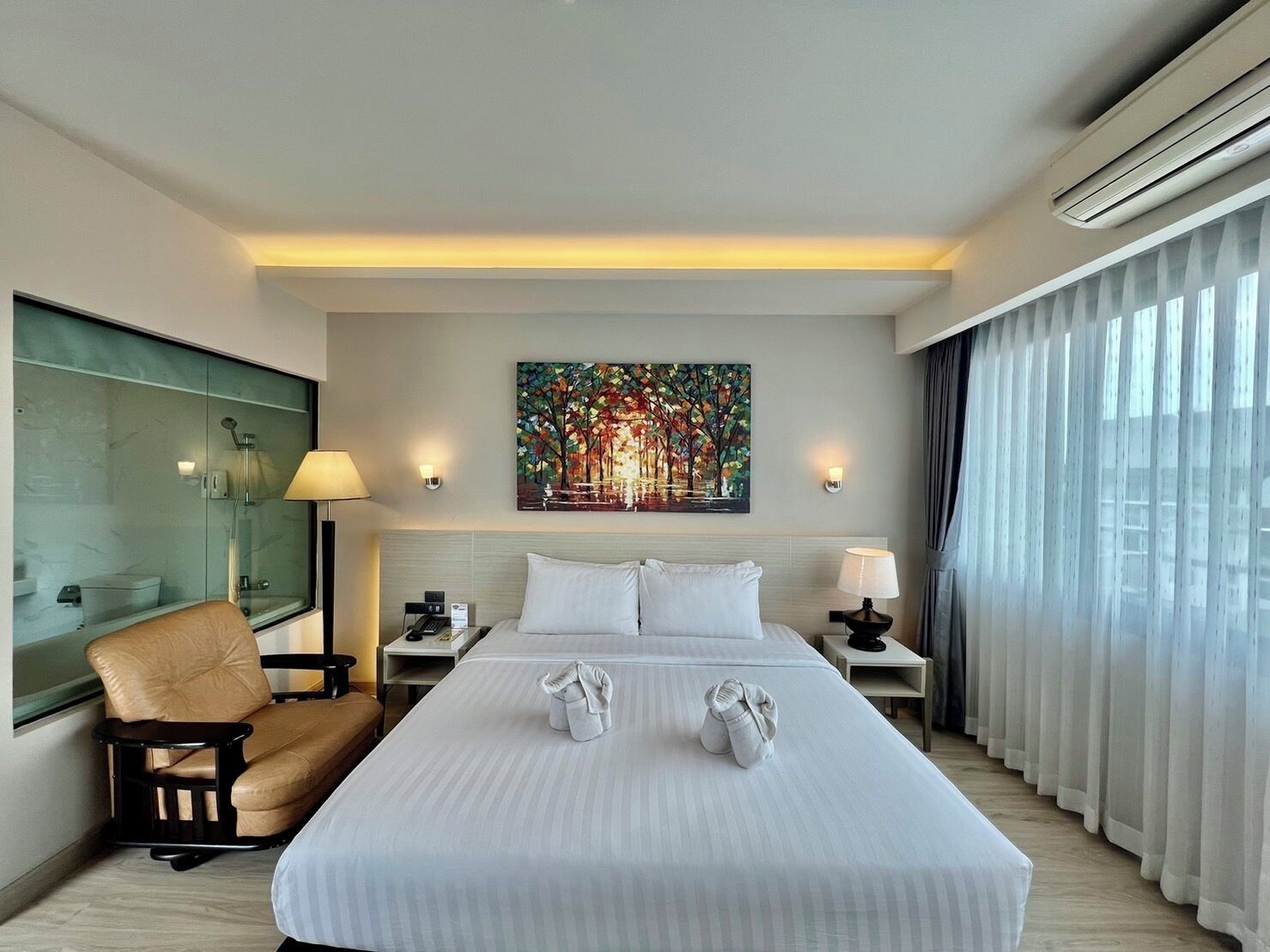 Quarto de hotel com uma cama grande, uma cadeira, um quadro e uma janela com cortinas.