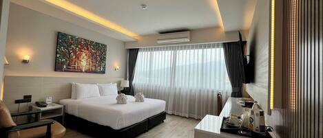 A modern hotel room with a large bed, a desk, a chair, a painting, and a TV.