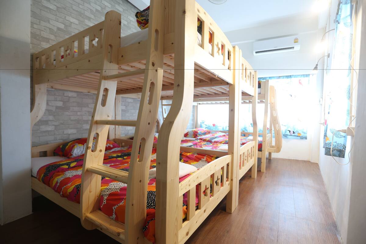 A bunk bed room with a brick wall, wooden flooring, and a window with a view.