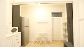 A compact kitchen with a microwave, refrigerator, and a small dining table with chairs. - Blue Jasmine Hostel (Bangkok)