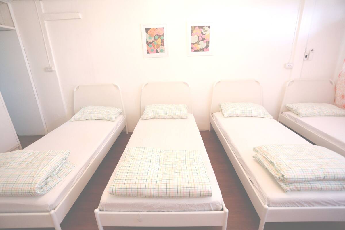 A room with three single beds, each with a checkered bedspread and matching pillows. There are two framed artworks on the wall above the beds.