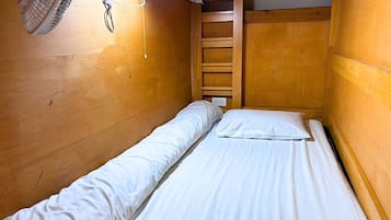Una habitación pequeña con cama individual, paredes de madera y ventilador de techo.