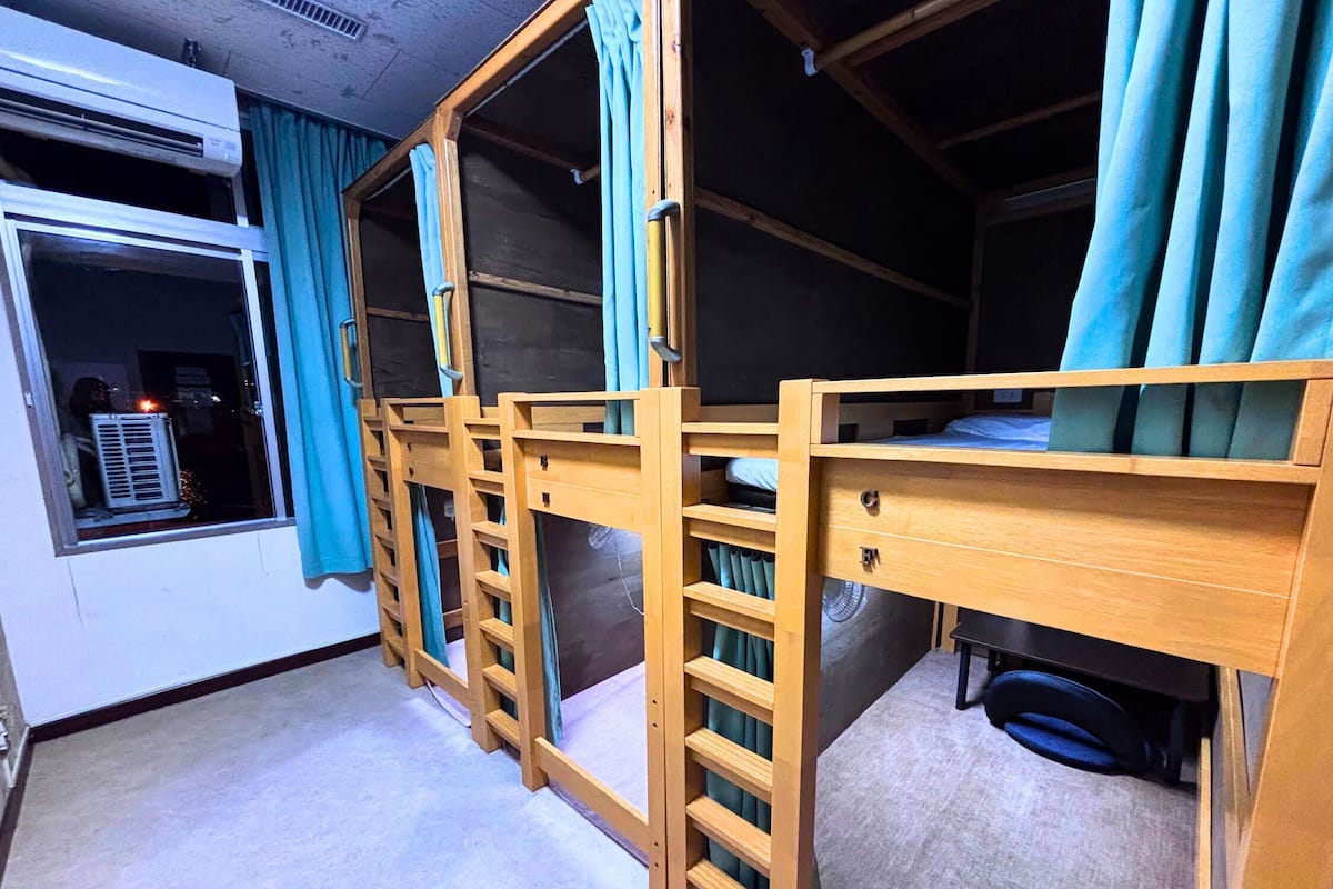 Una habitación con literas, una ventana con cortinas y un equipo de aire acondicionado.
